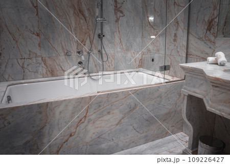Luxurious bathroom with marble walls, white bathtub, sink, and shower in Venice, Italy. Opulent space with no artwork or window, likely part of a high-end hotel or restaurant. 109226427