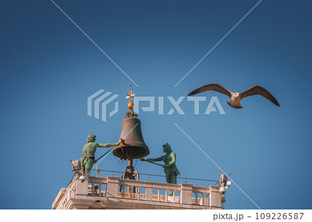 A stunning image of a seagull soaring over a bell tower in Venice, Italy, against a clear blue sky. The iconic tower adds charm to the peaceful, sunny summer scene. 109226587