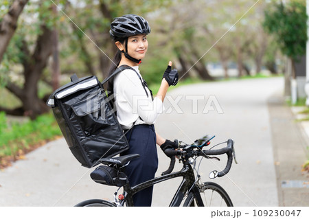 ロードバイクを前にしてデリバリーバックを背負って親指立てているフードデリバリー配達員の女性 の写真素材 [109230047] - PIXTA