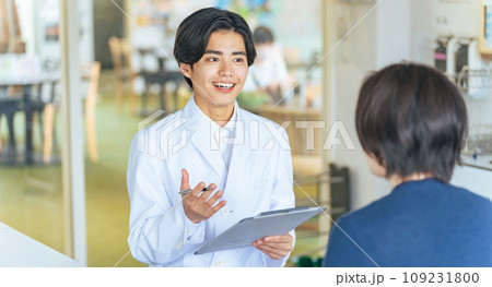 女性と会話する若い白衣の男性 医師 カウンセラー 女性と会話する若い白衣の男性 医師 カウンセラー 109231800