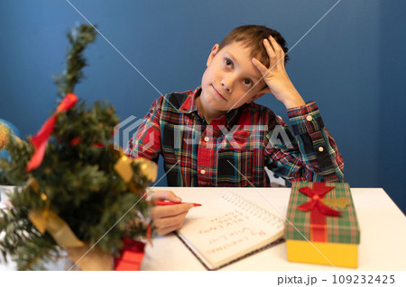 boy writing letter for Santa Claus for christmas sitting at the table at home 109232425