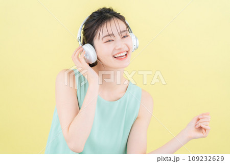イエローバックでヘッドフォンをつけて音楽を聴く若い女性 109232629