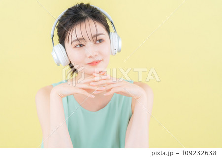 イエローバックでヘッドフォンをつけて音楽を聴く若い女性 109232638