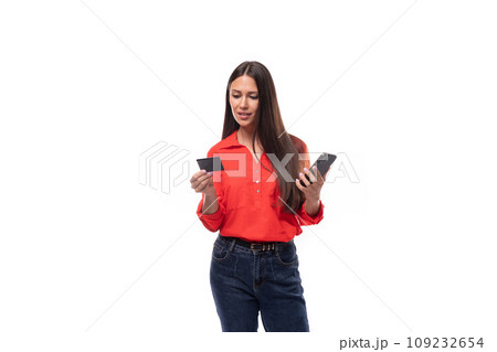 young caucasian brunette employee woman dressed in red blouse uses plastic card and smart phone 109232654
