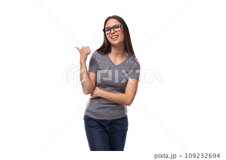 young positive brunette woman with glasses in a gray t-shirt with a mockup on a white background 109232694