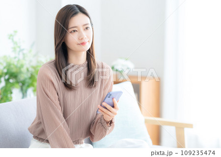 リビングのソファでスマホを使う若い女性 リビングのソファでスマホを使う若い女性 109235474