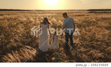Daughter with parents strolls across vast expanse of wheat in gentle breeze 109235689