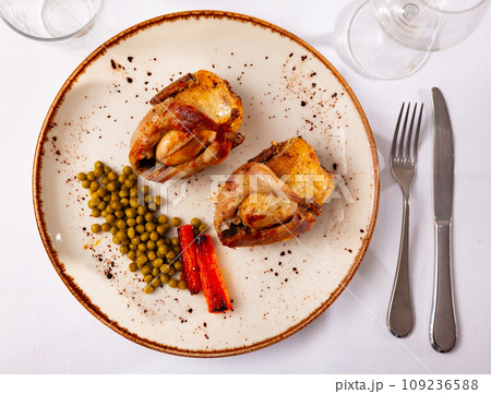 Roasted whole quails served on plate with peas and fried carrot 109236588