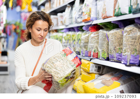 Woman take hay from shelf, inspect label in pet store. 109237093