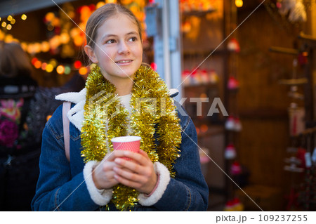 Teenagers girl holding hot cup of coffee in hands at street christmas fair Teenagers girl holding hot cup of coffee in hands at street christmas fair 109237255