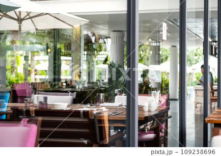 Hotel restaurant space with tables set for dinner at luxury resort, view through by window. Hotel restaurant space with tables set for dinner at luxury resort, view through by window. 109238696
