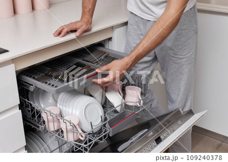 close-up, man loads plates into the dishwasher machine in the kitchen 109240378