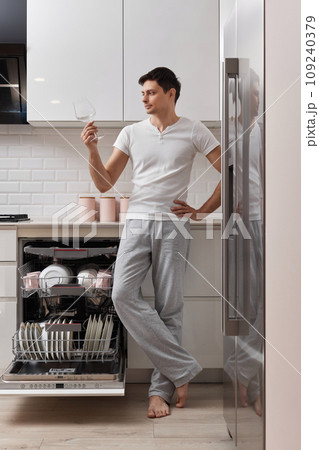 happy man taking out clean glass from dishwasher machine in the kitchen happy man taking out clean glass from dishwasher machine in the kitchen 109240379