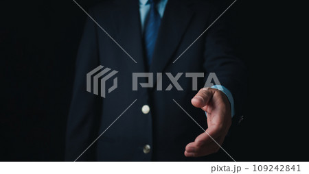 Businessman standing and doing handshake gesture on dark background. Business concept. Copy space. Businessman standing and doing handshake gesture on dark background. Business concept. Copy space. 109242841