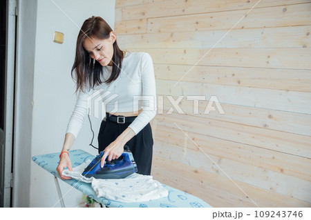 woman ironing things with an iron on an ironing board 109243746