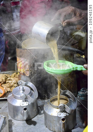 Tea maker hand pouring milk tea in pot after sieving with plastic sieve with another kettle by the side in Odisha, India, Asia,12.02.2020. Tea maker hand pouring milk tea in pot after sieving with plastic sieve with another kettle by the side in Odisha, India, Asia,12.02.2020. 109248195