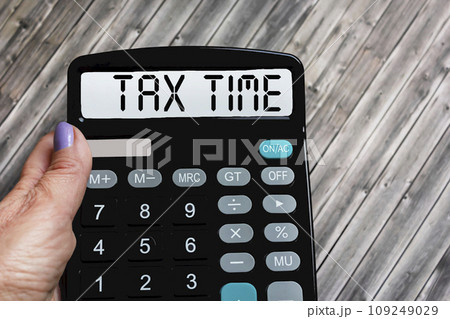 A woman's hand holds the word Tax time on a calculator. Business and taxation concept. A woman's hand holds the word Tax time on a calculator. Business and taxation concept. 109249029