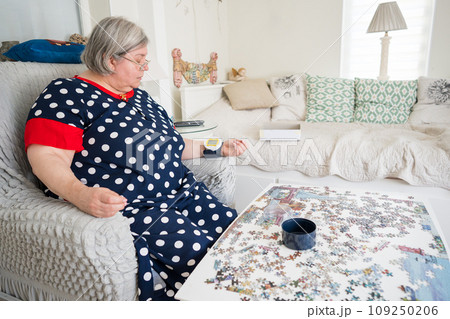 Senior woman measuring blood pressure and pulse using medical electronic tonometer while sitting on armchair at bright home room. An elderly woman overweight and hypertension problems. Senior woman measuring blood pressure and pulse using medical electronic tonometer while sitting on armchair at bright home room. An elderly woman overweight and hypertension problems. 109250206