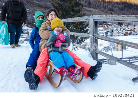 father with three daughters going down on snow slope with wooden sled 109250421