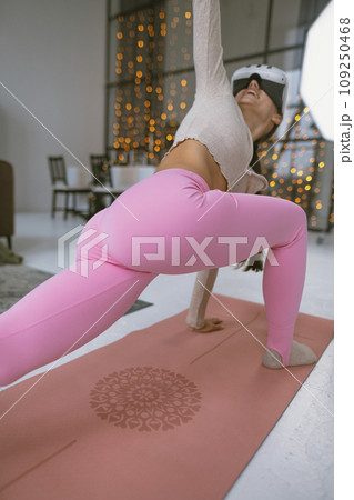 Exercising in a pink sports outfit with a virtual reality headset amidst a Christmas tree's backdrop. Exercising in a pink sports outfit with a virtual reality headset amidst a Christmas tree's backdrop. 109250468