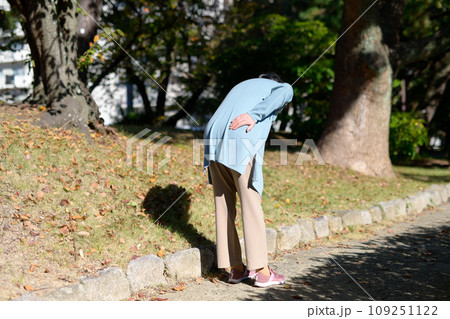 腰の痛みを訴えるシニアの女性　高齢者　腰痛　臀部の痛み　心配不安　散歩　うつむく 109251122