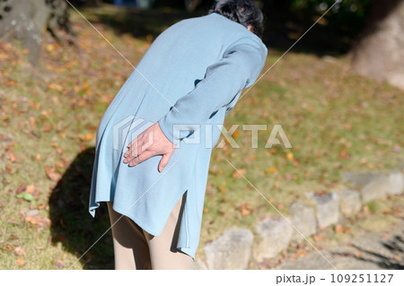 腰の痛みを訴えるシニアの女性　高齢者　腰痛　臀部の痛み　心配不安　散歩　うつむく 109251127