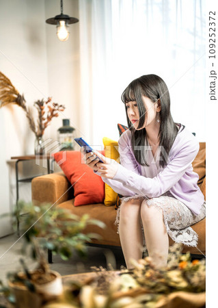 ソファーに座りながらスマホをいじるロングヘアの女性 ソファーに座りながらスマホをいじるロングヘアの女性 109252372