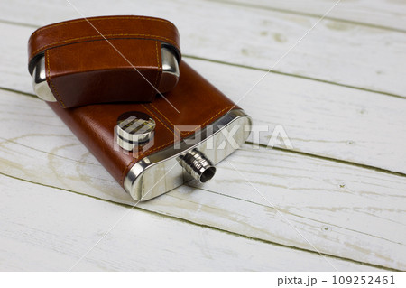 An open leather flask for alcohol with leather trim lies on a white wooden table An open leather flask for alcohol with leather trim lies on a white wooden table 109252461