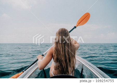 Woman in kayak back view. Happy young woman with long hair floating in transparent kayak on the crystal clear sea. Summer holiday vacation and cheerful female people relaxing having fun on the boat 109254755
