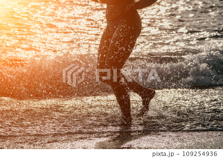 Running woman on a summer beach. A woman jogging on the beach at sunrise, with the soft light of the morning sun illuminating the sand and sea, evoking a sense of renewal, energy and health. 109254936