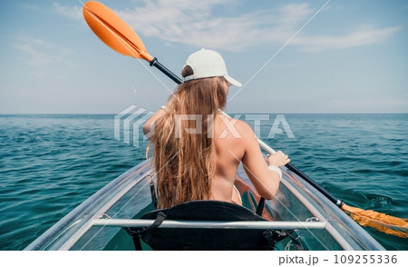 Woman in kayak back view. Happy young woman with long hair floating in transparent kayak on the crystal clear sea. Summer holiday vacation and cheerful female people relaxing having fun on the boat Woman in kayak back view. Happy young woman with long hair floating in transparent kayak on the crystal clear sea. Summer holiday vacation and cheerful female people relaxing having fun on the boat 109255336