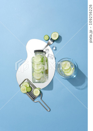 Top view of unbranded water bottle placed on a mirror. A glass filled with cucumber detox water displayed. Cucumber (Cucumis sativus) is one of the natural ingredients Top view of unbranded water bottle placed on a mirror. A glass filled with cucumber detox water displayed. Cucumber (Cucumis sativus) is one of the natural ingredients 109256226