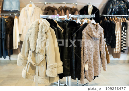 Beige coat with fur collar and sleeves hanging on stand in clothing store 109258477
