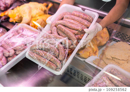 Container with sausages held in hands by seller against background of showcase of butcher shop 109258562