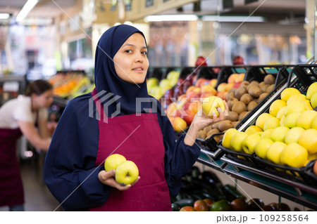 Young woman in hijab selling apples in grocery store 109258564