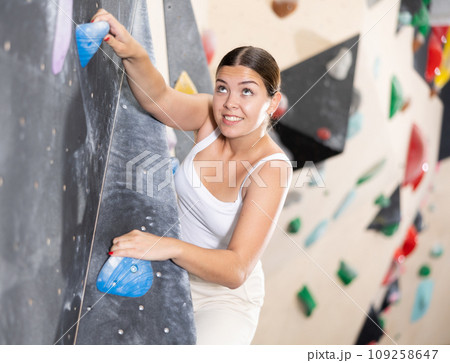 Sporty woman climbing on bouldering wall demonstrating physical strength, technical skill, and determination 109258647