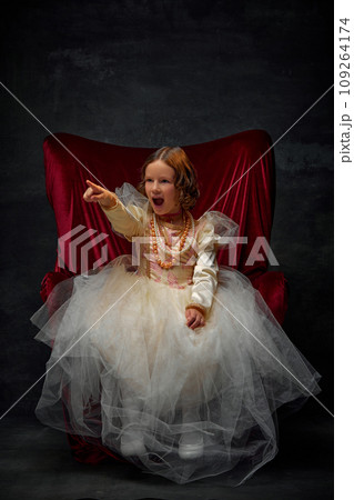 Get out. Little girl sitting on throne wearing in old-fashioned dress like princess and shouting threatening someone against dark vintage background. Get out. Little girl sitting on throne wearing in old-fashioned dress like princess and shouting threatening someone against dark vintage background. 109264174