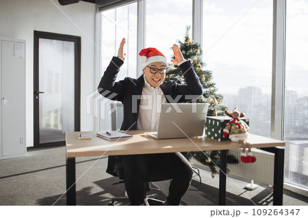 Emotional adult in Santa hat lifting hands while looking at computer screen Emotional adult in Santa hat lifting hands while looking at computer screen 109264347