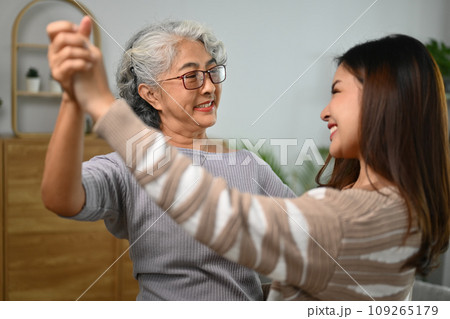 Happy gray haired middle age mother dancing with grown up daughter in living room 109265179