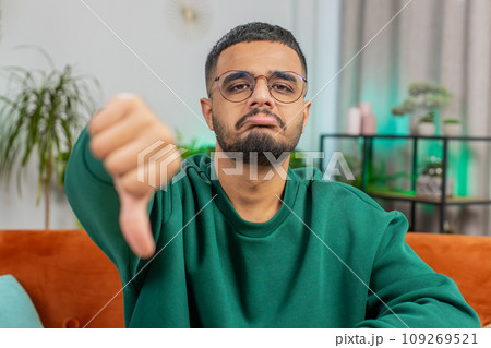 Upset Arabian man showing thumbs down, dislike bad work, disapproval dissatisfied feedback at home 109269521