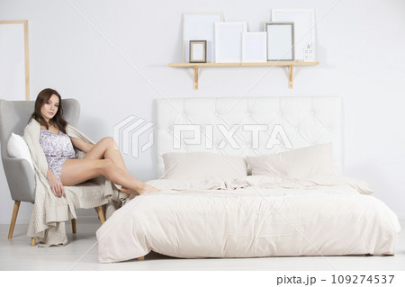 Girl in pajamas sits in a chair in a bright bedroom Girl in pajamas sits in a chair in a bright bedroom 109274537