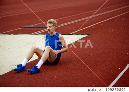 Full length portrait of man sitting on court and warming-up before championship. anticipation of athlete sportsman before crucial leap. Full length portrait of man sitting on court and warming-up before championship. anticipation of athlete sportsman before crucial leap. 109276845
