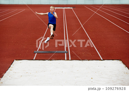 Athlete's body language in mid-air grace. Young man, professional sportsman pushed off ground hard and flew high to make perfect long jump 109276928