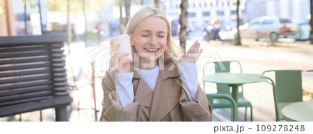 Portrait of cheerful young blond woman, enjoying spending time in outdoor cafe, drinking coffee and laughing, having casual meet up in street restaurant 109278248