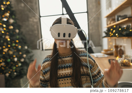 Utilizing a virtual reality headset, a beautiful and stylish girl prepares a Christmas recipe in the kitchen. Utilizing a virtual reality headset, a beautiful and stylish girl prepares a Christmas recipe in the kitchen. 109278617