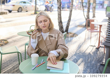 Portrait of serious, concentrated woman, opens her notebook, records voice message, sending notification to coworker, drinking coffee, working outdoors 109279354