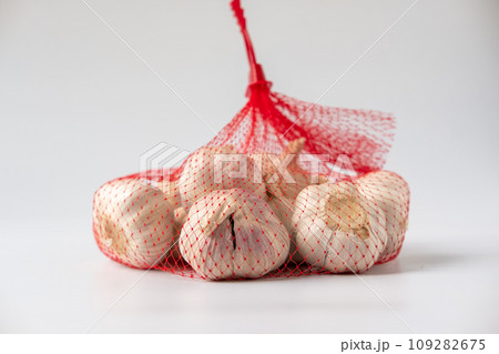 A large head of garlic is in a red mesh package on a white background. A large head of garlic is in a red mesh package on a white background. 109282675