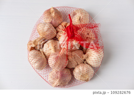 A large head of garlic is in a red mesh package on a white background. 109282676