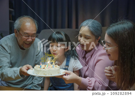Birthday surprise. Happy Asian family grandparents and mother celebrating enjoy birthday party with cake of granddaughter at home in night time 109282894