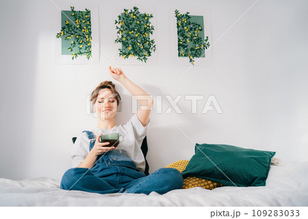 Woman with closed eyes listen music and enjoy cup of coffee or tea. Calm female spend free time at home enjoy favourite song with wireless modern headphones. Pastime weekend relax, no stress concept. 109283033